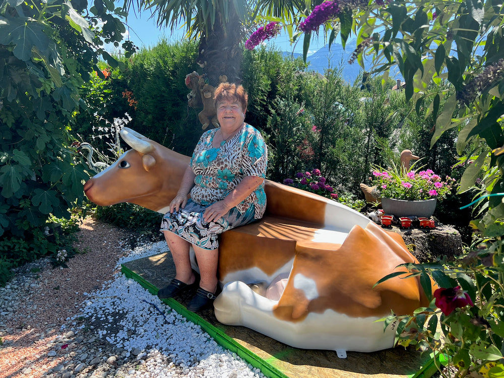Vache-banc Kuhtag couchée dans un jardin fleuri