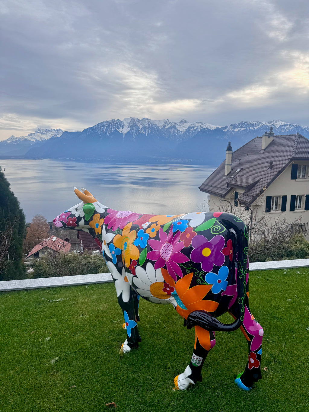 Vache Kuhtag à fleurs fond noir dans un jardin avec vue sur le Léman