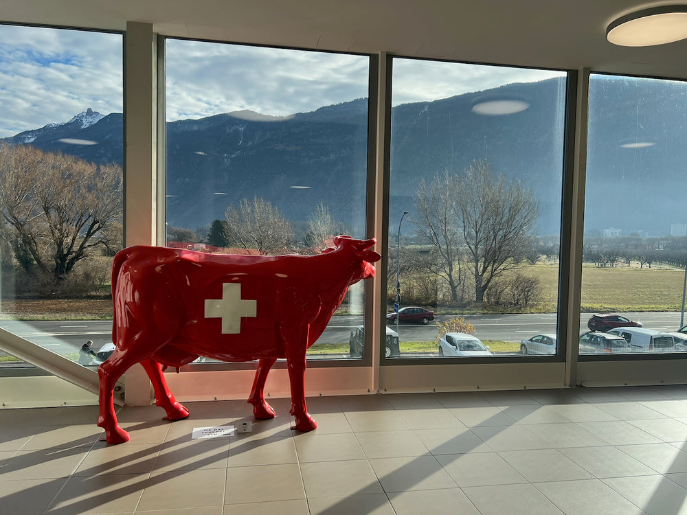 Vache Kuhtag à croix suisse dans un hall vitré face aux montagnes